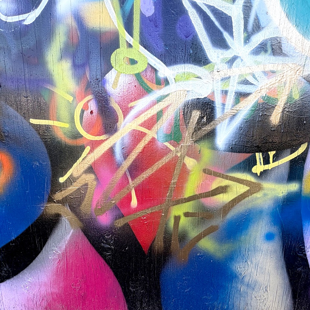 Close-up of colorful graffiti featuring abstract shapes and lines in various colors, including pink, blue, and yellow.